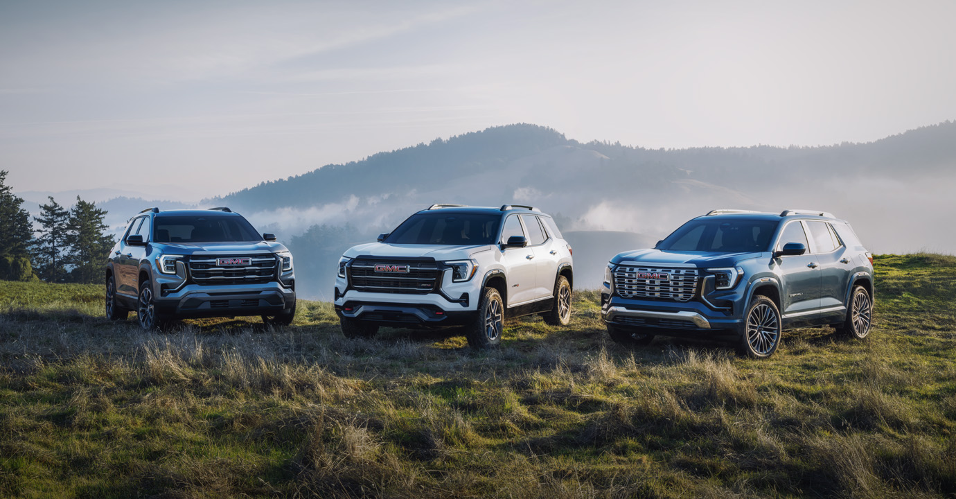 Three GMC SUVs parked in the grass with a view of forested mountains behind them.